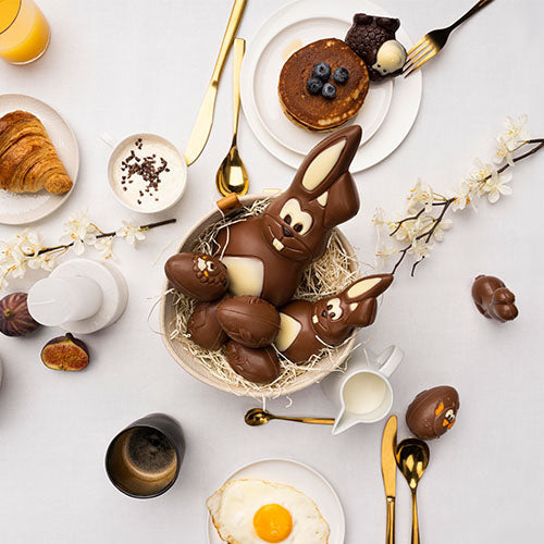 Feestelijk paasontbijt met chocolade paashazen en paaseitjes, omringd door croissants, pannenkoeken en koffie