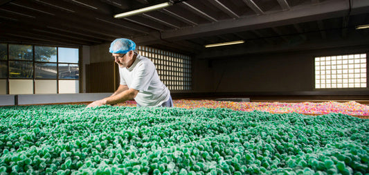 Medewerker controleert groene gesuikerde snoepjes tijdens het productieproces in een snoepfabriek